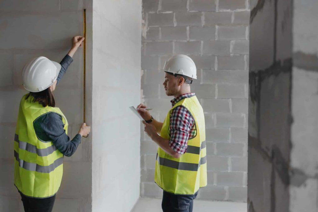 Illustration pour l'article Plan de prévention en entreprise : pourquoi, quand et comment le rédiger ? Cette image montre deux travailleurs portant des casques jaunes qui travaillent côte à côte sur un site de construction.
